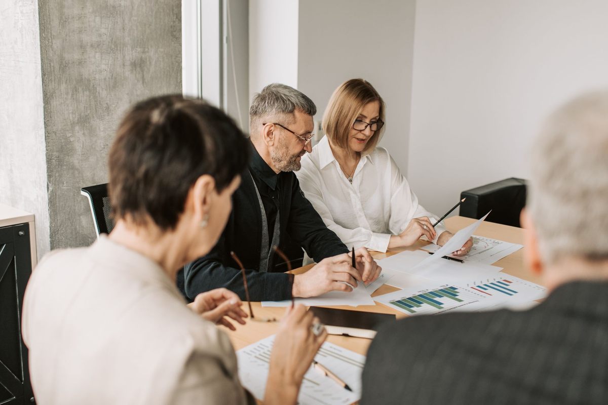 Groupe de professionnels en réunion analysant des documents et graphiques sur une table Groupe de professionnels en réunion analysant des documents et graphiques sur une table