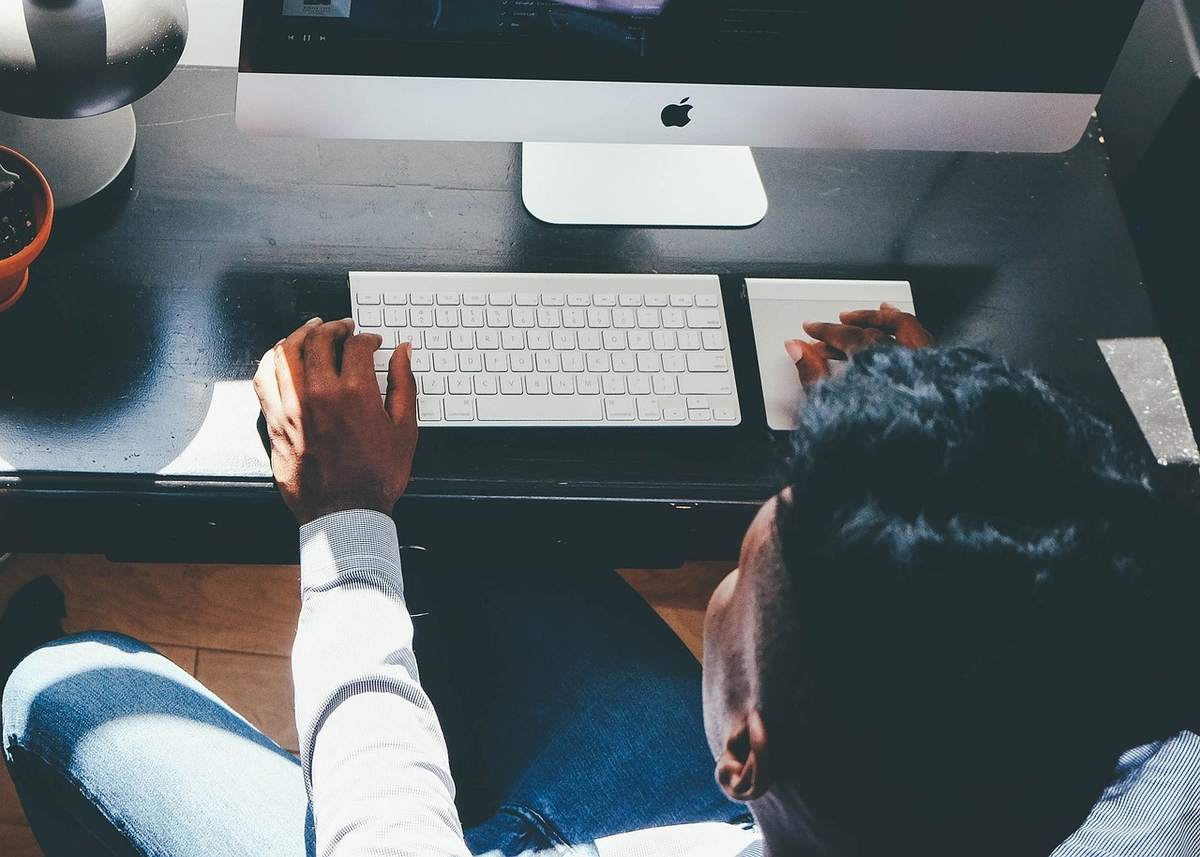 Person seated, hands on keyboard and mouse, looking at iMac screen
